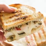 Hand holding half of a pesto chicken sandwich on sourdough.