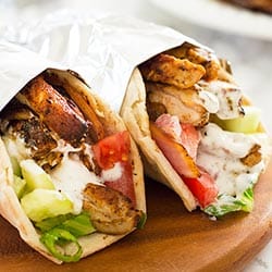 Chicken shawarma with yogurt shawarma sauce wrapped in foil on a wooden plate.