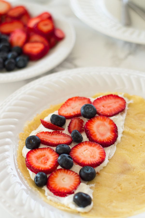 Crepe being filled with whipped cream and fruit.