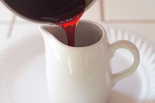 Strawberry syrup being poured into a small white pitcher.