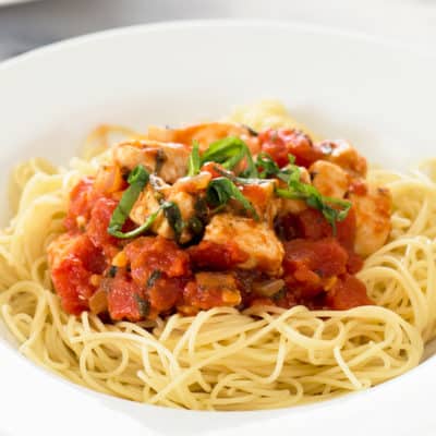 Photo of Basil Chicken Pasta over angel hair pasta in a white bowl.