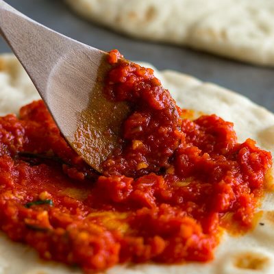 Homemade pizza sauce being spread on naan pizza.