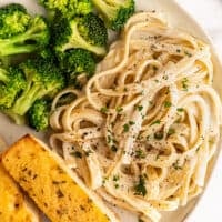 Fettuccine alfredo for one on a plate with broccoli and garlic bread.