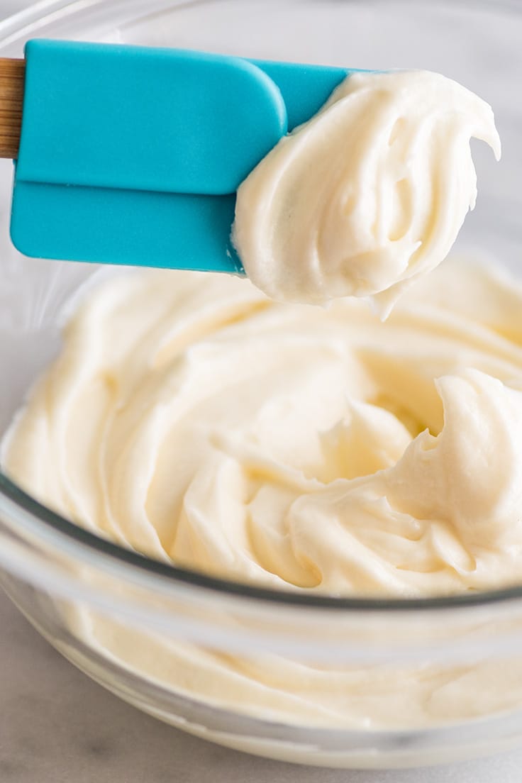 Cream cheese frosting being scooped out of a glass bowl.