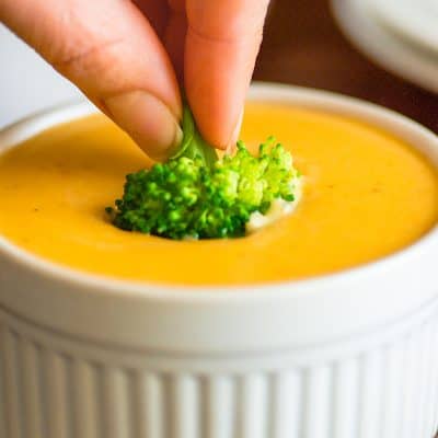Piece of broccoli being dipped in cheese sauce.