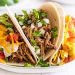 Three different types of carnitas tacos on a plate.
