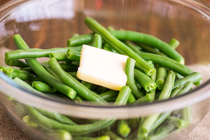 Image of How to Steam Green Beans in the Microwave step 3, green beans in a bowl with tab of butter.
