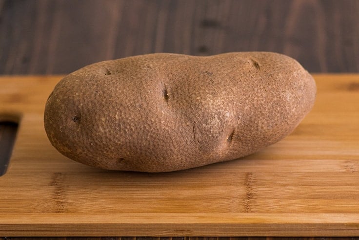 Mashed Potatoes for Two Photo Step 1: russet potato on a cutting board reading to be peeled and cut.