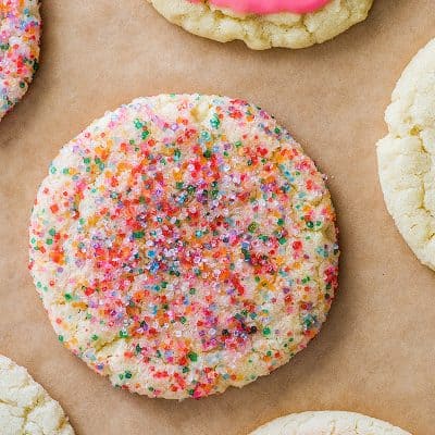 Small-batch Sugar Cookies rolled in rainbow sprinkles and glazed on parchment paper.