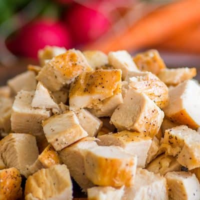 Cooked chicken breasts cubed on a cutting board.