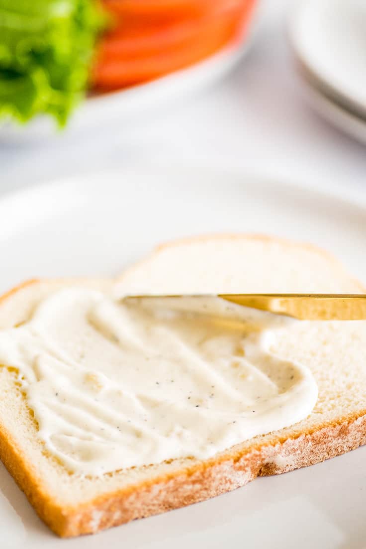Photo of garlic aioli being spread on a sandwich.