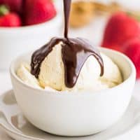 Nutella sauce being poured over ice cream in a white bowl.