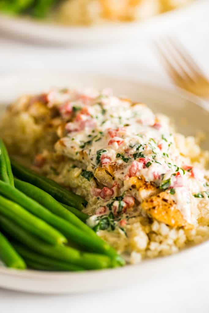 Close up image of keto chicken over cauliflower rice with cream sauce on a plate with green beans.