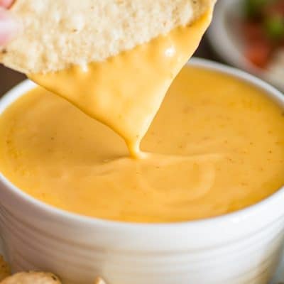 Picture of tortilla chip being dipped into homemade nacho cheese.