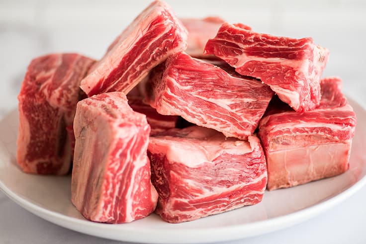 Picture of raw short ribs on a white plate.