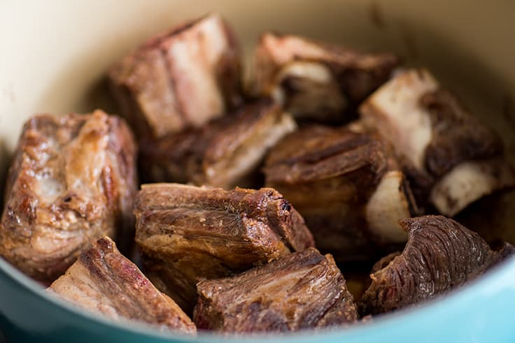 Image of browned short ribs for braising in a blue pot.