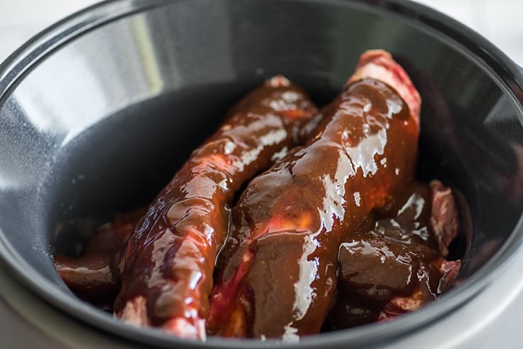 Beef ribs in a slow cooker with barbecue sauce.