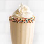 Vanilla milkshake in a glass cup with sprinkles around the rim.