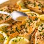 Spooning white wine lemon butter sauce over chicken breast in a skillet.