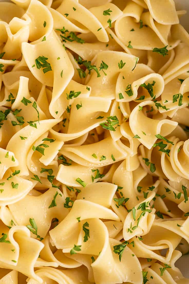 Very close up photo of buttered noodles sprinkled with parsley.