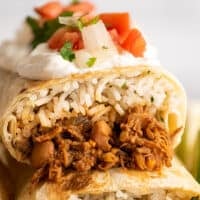 Close up photo of shredded beef burritos stacked.