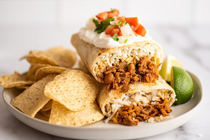 Shredded beef burritos on a white plate with tortilla chips.