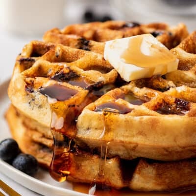 Blueberry waffles stacked on a plate with butter and syrup.