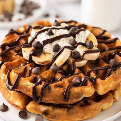 Chocolate chip waffles with banana slices, whipped cream, and chocolate sauce on a white plate.