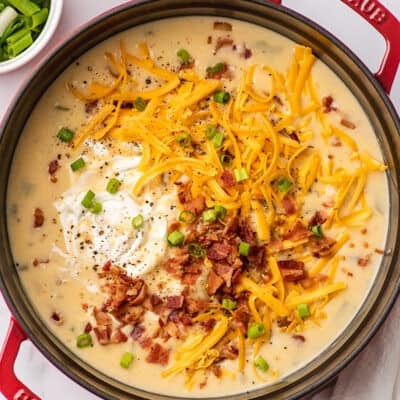 Potato bacon soup topped with cheese, bacon, and sour cream in a pot.