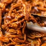 BBQ shredded chicken being picked up with tongs.