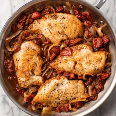 Balsamic chicken in a skillet with tomatoes and onions.
