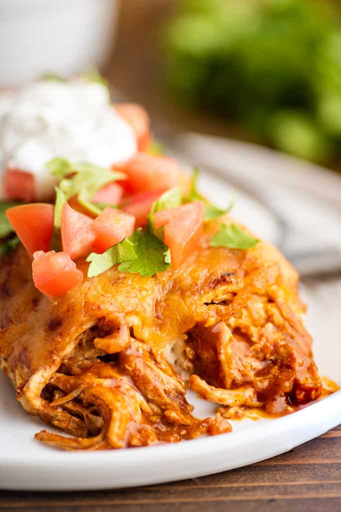 Close photo of chicken enchiladas with sour cream on a plate.