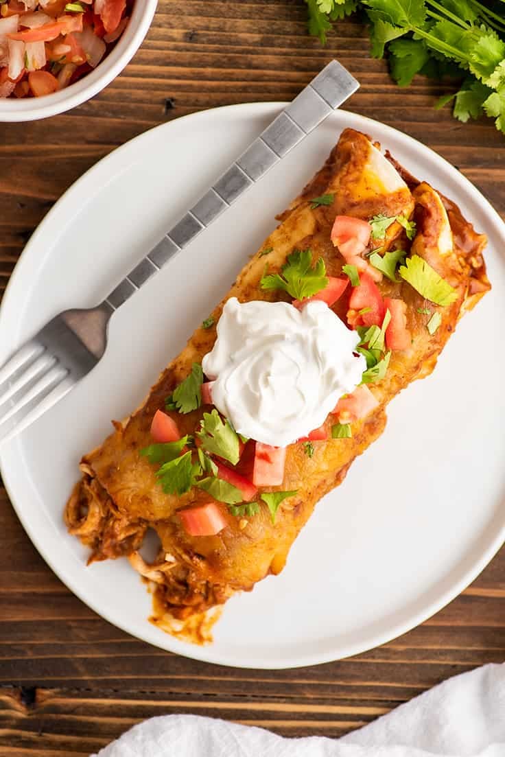 Overhead photos of chicken enchiladas on a plate with sour cream on top.