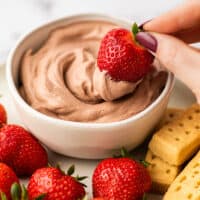 Strawberry being dipped into chocolate whipped cream.