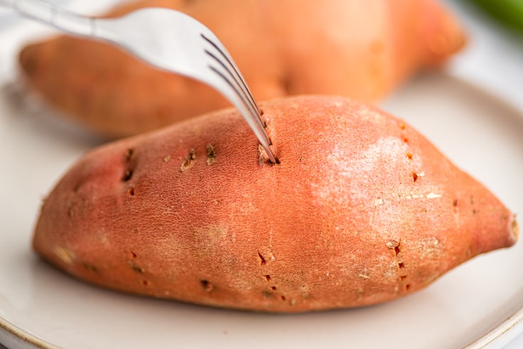 Sweet potato being pierced with a fork for microwaving.