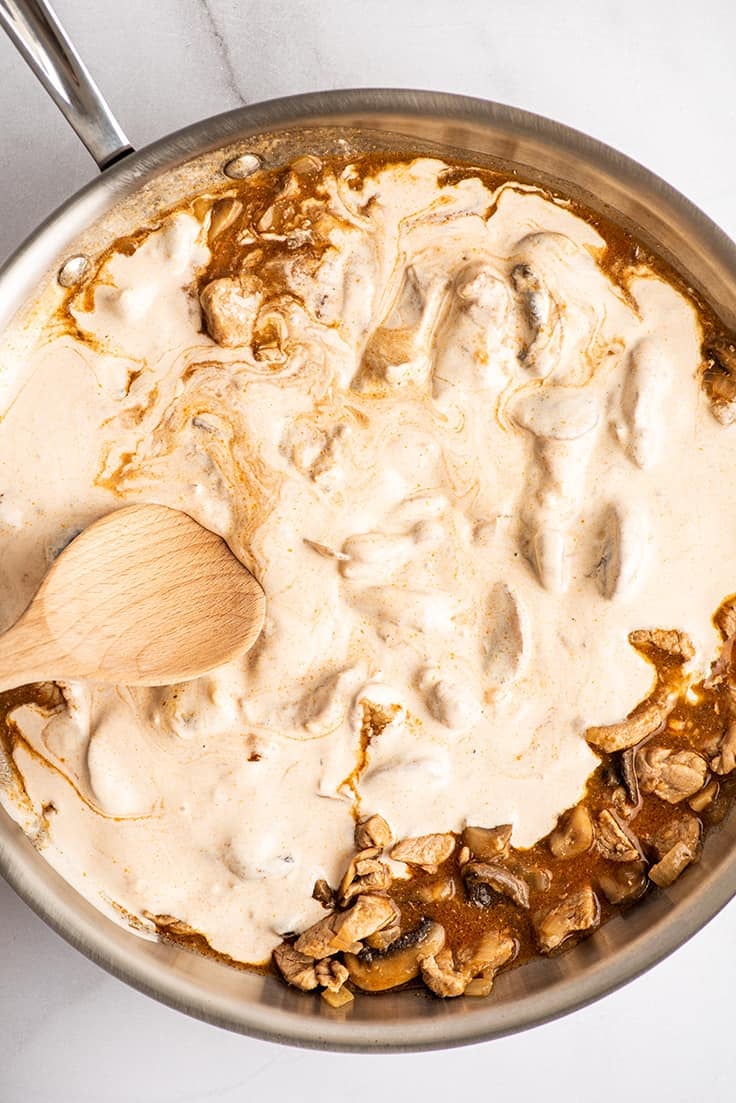 Tempered sour cream being stirred into pork stroganoff.