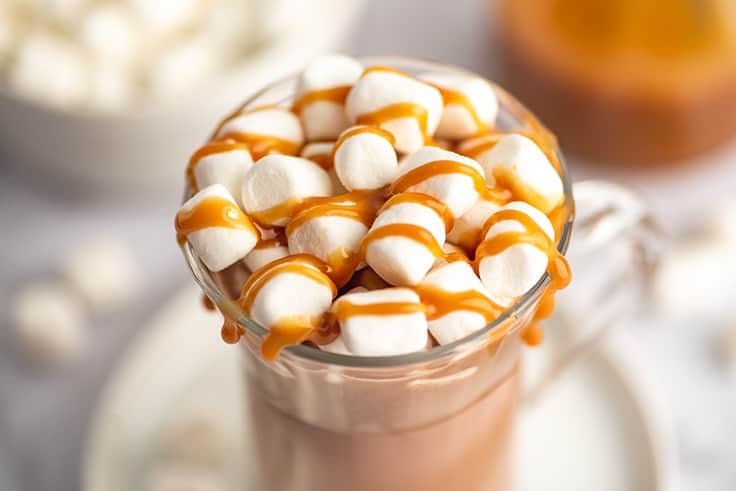 Close photo of salted caramel hot chocolate in a mug with marshmallows and caramel drizzle.