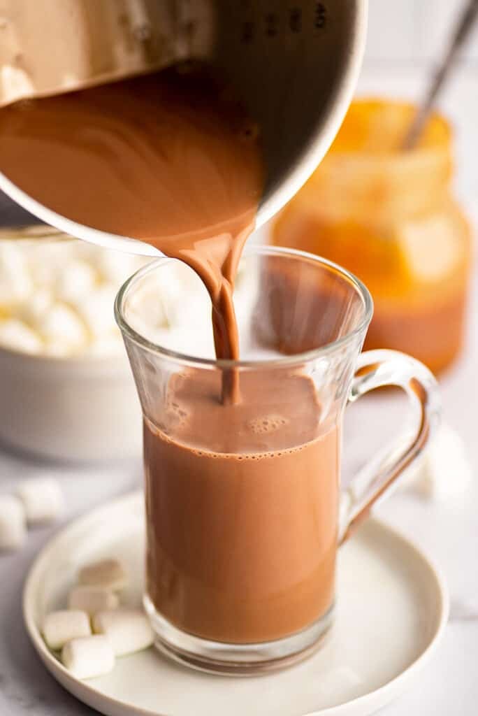 Salted caramel hot chocolate being poured into a glass mug.