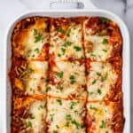 Photo of lasagna in a white dish with parsley on top.