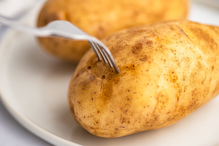 Potato being pierced with a fork before microwaving. 
