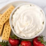 Bowl with cream cheese whipped cream next to strawberries.