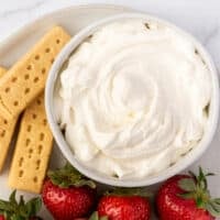 Bowl with cream cheese whipped cream next to strawberries.