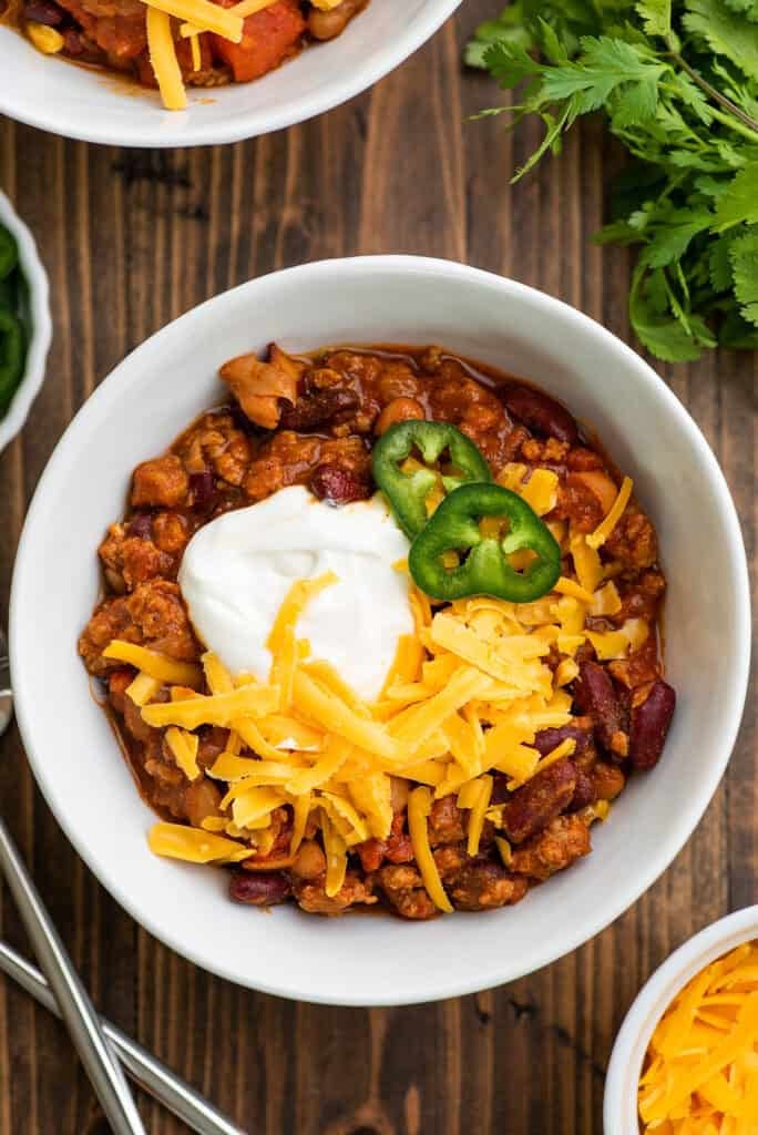 a bowl of Ground Turkey Chili topped with sliced jalepenos, sour cream, and shredded cheese