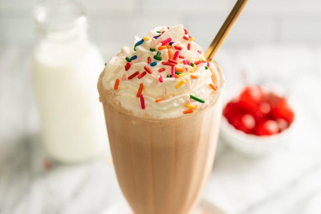 Malted milkshake in a glass with sprinkles and whipped cream.