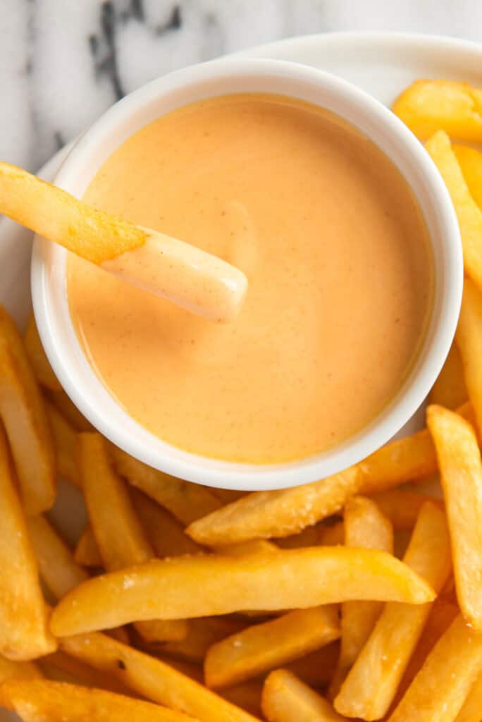 Close up of a fry dipping into Sriracha aioli