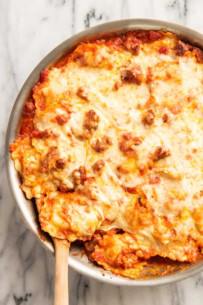 Baked ravioli being spooned out of a pan.