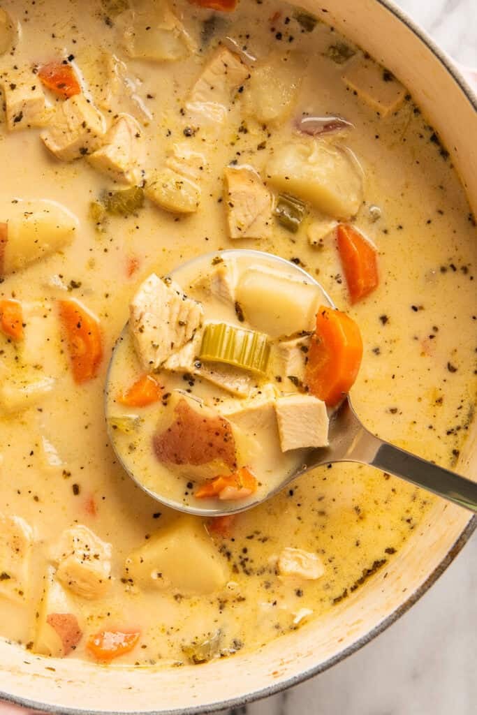 Close up of creamy chicken and potato soup being ladled out of a pot.