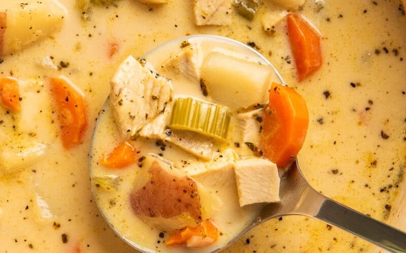 Close up of creamy chicken and potato soup being ladled out of a pot.