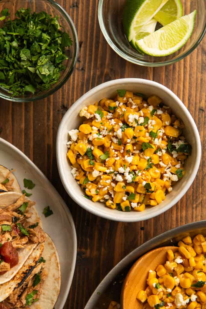 A white bowl filled with corn with cilantro, lime, and cheese