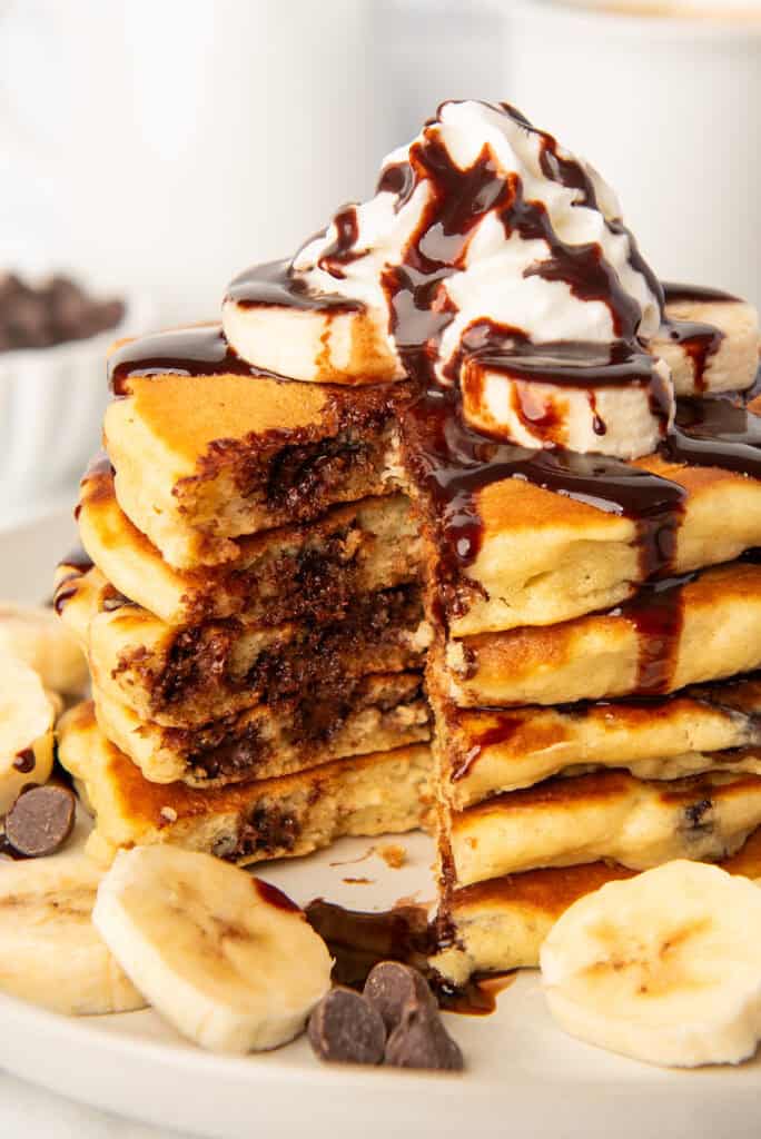 Close up photo of chocolate chip pancakes with whipped cream and chocolate sauce